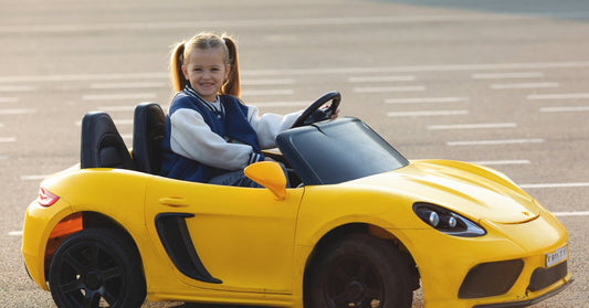 A close-up of a young girl smiling while sitting in a yellow ride-on car that is parked on lined pavement.