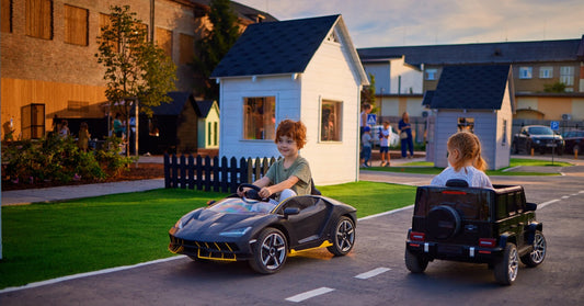 Two young children riding in electric ride-on cars going in opposite directions. They are riding on a small playground road.