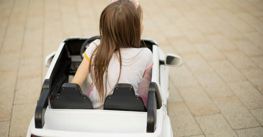 A young girl sitting in a white electric ride-on car for kids. The car is parked on a brick surface.