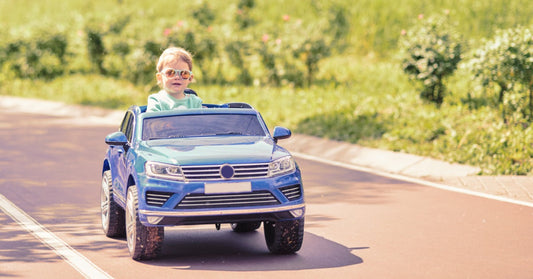 A close-up of a young child wearing sunglasses while driving a blue ride-on car along an outdoor path.