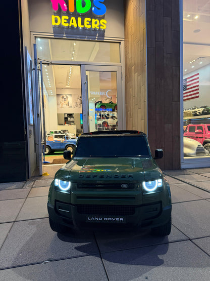 A dark green Land Rover Defender toy car parked in front of a children's toy dealership storefront at night.