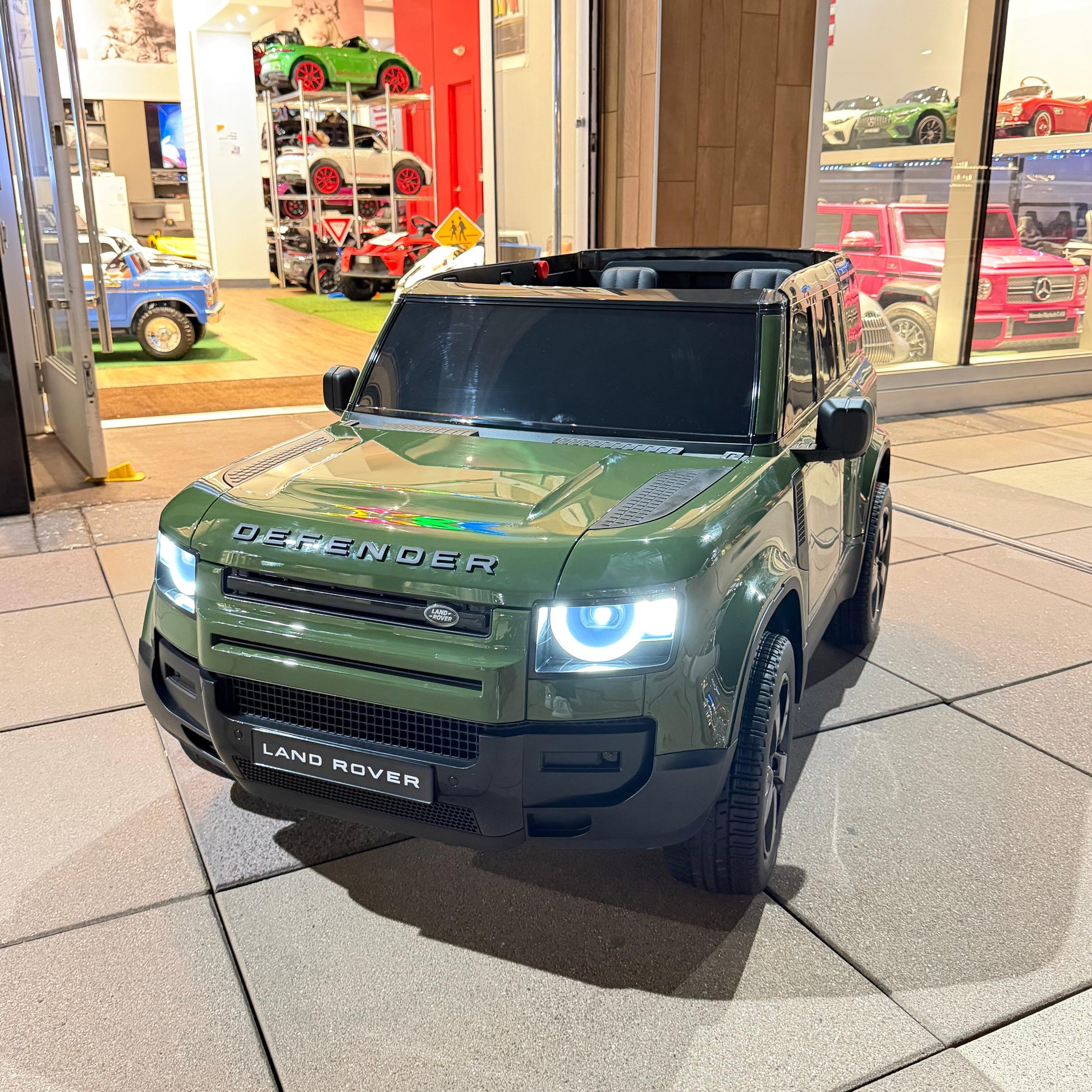 A green toy SUV car styled like a Land Rover Defender, parked indoors on a tiled floor
