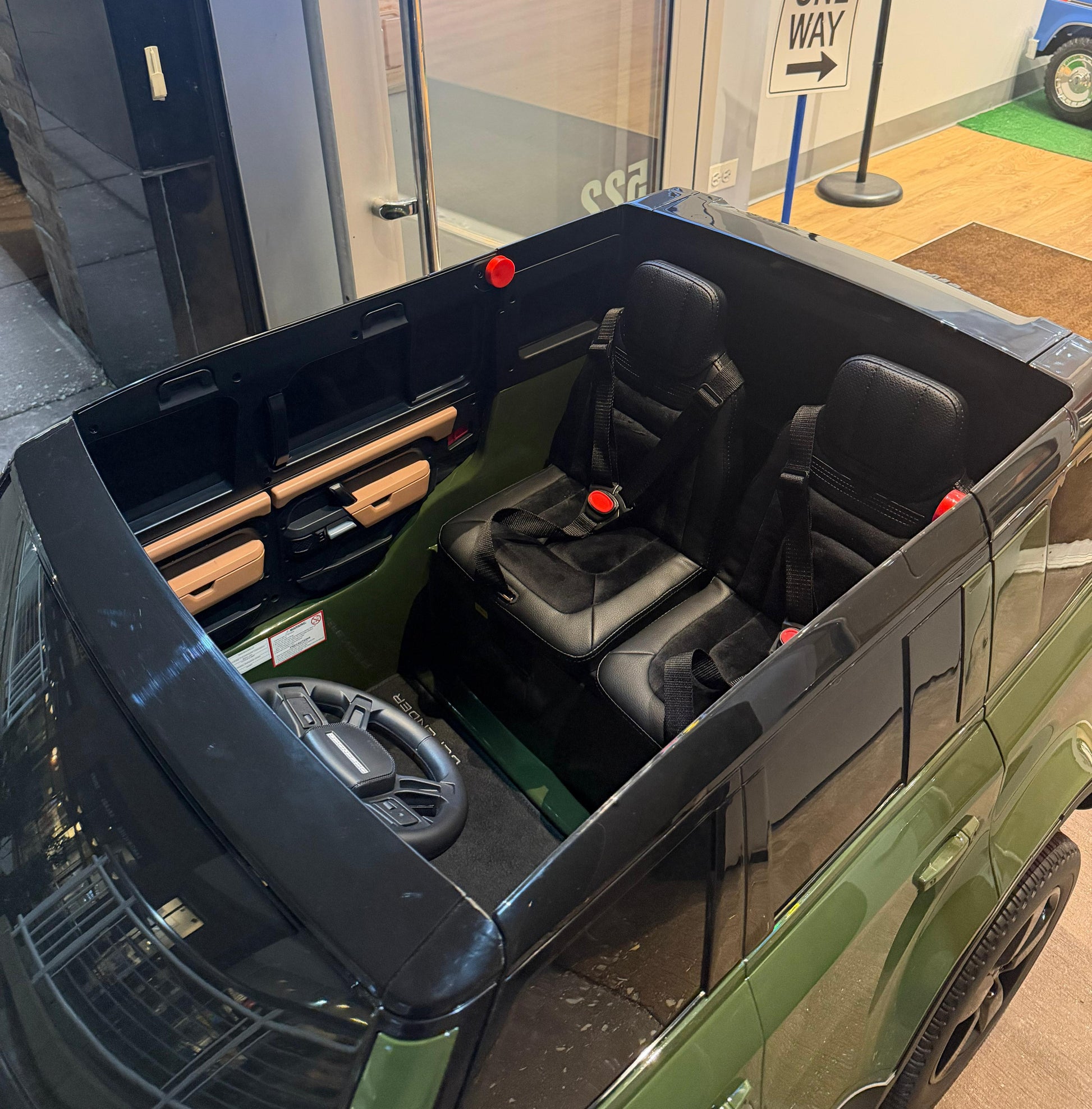 A green and black ride-on toy SUV shown from an elevated angle, featuring two black front seats with seatbelts