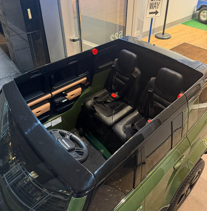 A green and black ride-on toy SUV shown from an elevated angle, featuring two black front seats with seatbelts